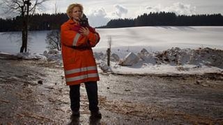 Bea steht in Feuerwehrmontur in Schneelandschaft und hat eine in eine Decke gewickelte schwarzgraue Katze auf dem Arm