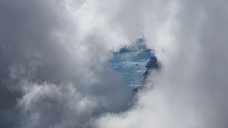 Nebel zieht rasch auf und lässt nur noch durch ein Wolkenfenster einen Blick auf den See zu.