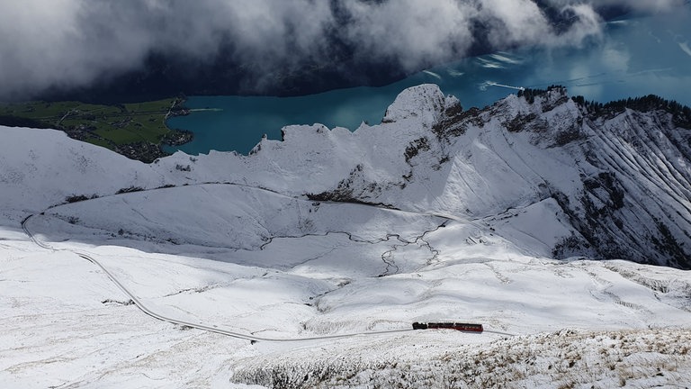 Im Wechselspiel des Wetters hat es am Morgen geschneit und die Zahnradstrecke ist von der Bergstation nur noch als dünne schwarze Schleife zu erkennen.