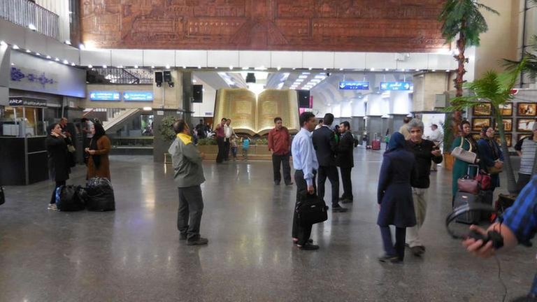 Bahnhofshalle in Teheran, im Hintergrund ein übergroßer Koran