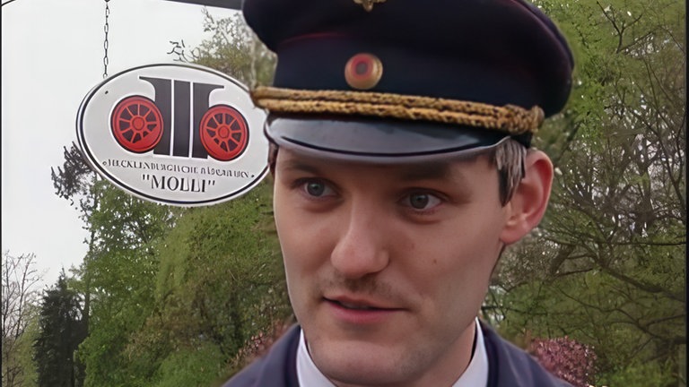 Ein Mitarbeiter redet vor einem "Molli"-Schild mit Eisenbahn-Romantik