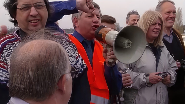 Ein Mann mit Megaphon hält eine Ansprache an die Fahrgäste.