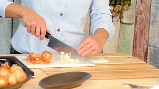 Zwiebeln werden auf einem Brettchen klein gehackt