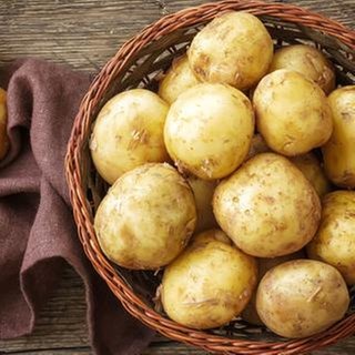 Pellkartoffeln mit Schale liegen in einem geflochtenen Korb auf einem Holztisch.