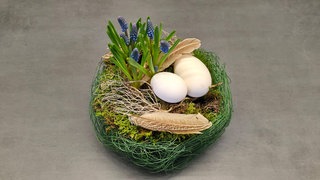 Osterkorb mit Frügblühern, Eierschalen und Federn