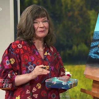 Cornelia Richter steht neben einem Bild auf einer Leinwand.
