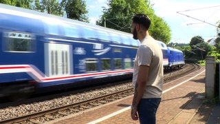 Sasho Sashev überlebt 15.000 Volt-Stromschlag. Er steht an den Gleisen neben einem vorbeifahrenden Zug.