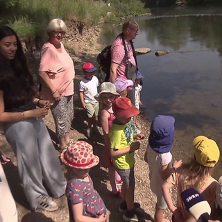 Kinder stehen am Ufer und werfen eine Flaschenpost ins Wasser