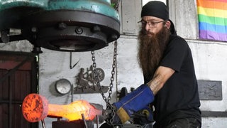 Schmied Timo Eigenmann formt mit einem Werkzeug ein glühendes Werkstück in seiner Schmiede.