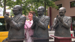 Moderatorin Sonja Faber-Schrecklein steht bei der Skulptur „Die Claque“ in Flein und applaudiert mit den Figuren.