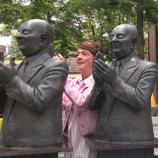 Moderatorin Sonja Faber-Schrecklein steht bei der Skulptur „Die Claque“ in Flein und applaudiert mit den Figuren.