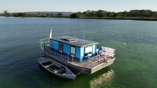 Hausboot „Netta“ schwimmt mitten im Bodensee zwischen Wasservögeln.
