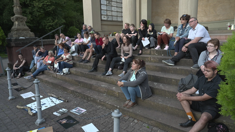 Eine Gruppe von Menschen sitzt auf einer Treppe im Freien und schaut aufmerksam in den abendlichen Himmel, gespannt auf Fledermäuse.
