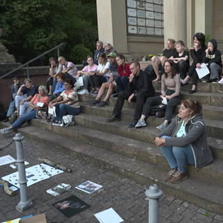Eine Gruppe von Menschen sitzt auf einer Treppe im Freien und schaut aufmerksam in den abendlichen Himmel, gespannt auf Fledermäuse.