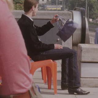 Ein Mann sitzt auf einem Stuhl und hält eine kleine Handtasche in der Hand.