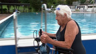 Die 101 Jahre alte Else Spiesberger geht fast jeden Tag im Freibad schwimmen. Sie trägt einen Badeanzug und nutzt eine Gehhilfe.