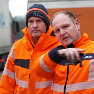 Drei Männer der Autobahnmeisterei stehen auf der Autobahn.