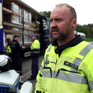 Verkehrskontrolle der Autobahnpolizei auf der A81: ein LKW-Fahrer wird kontrolliert. Im Vordergrund steht ein Polizist in gelber Warnweste.