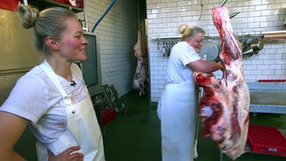 Die Metzgerinnen Sonja und Chantal. Sonja schaut Chantal zu, wie sie Fleisch verarbeitet.