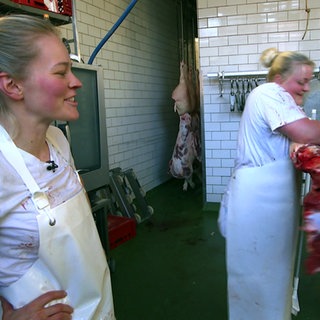 Die Metzgerinnen Sonja und Chantal. Sonja schaut Chantal zu, wie sie Fleisch verarbeitet.