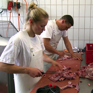 In einer Metzgerei in Lauffen am Neckar arbeiten Metzgerein Sonja und ein Mann in der Küche. Sie schneiden rohes Fleisch.