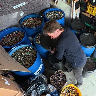 Joachim Jantzen aus St. Georgen im Schwarzwald steht zwischen Fässern voller Kronkorken. Er sammelt sie für einen guten Zweck.