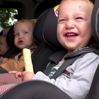 Drillinge sitzen auf der Rückbank in ihren Babyschalen im Auto.