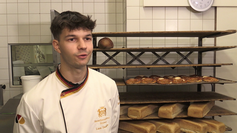 Brezelkönig Luca Stadelhofer steht in der Bäckerei und spricht in die Kamera.