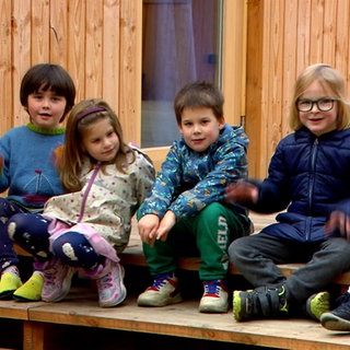 Kinder der Kita Knopfschachtel sitzen auf einer Holzttreppe im Freien.