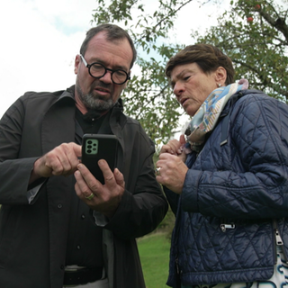 Sonja Faber-Schrecklein und Markus Hölz stehen auf einer Streuobstwiese in Mössingen und schauen auf ein Handy. 