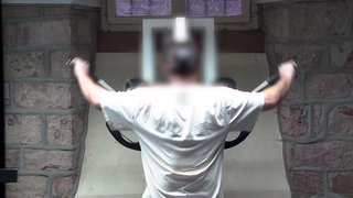 Ein Insasse der JVA Mannheim ist im Sportraum und trainiert an einem Gerät. Er ist von hinten zu sehen.