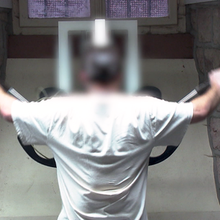 Ein Insasse der JVA Mannheim ist im Sportraum und trainiert an einem Gerät. Er ist von hinten zu sehen.