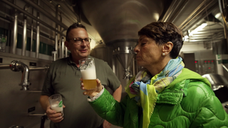 Sonja Faber-Schrecklein und Tobias Fischer stehen in einer Brauerei. Beide halten ein Bierglas in der Hand.