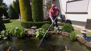 Thomas Taller steht mit einem Kescher an seinem Koiteich im Garten.
