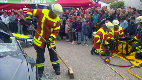 Vier Feuerwehrmänner zeigen einem Publikum einen Feuerwehreinsatz. 
