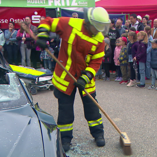 Vier Feuerwehrmänner zeigen einem Publikum einen Feuerwehreinsatz. 