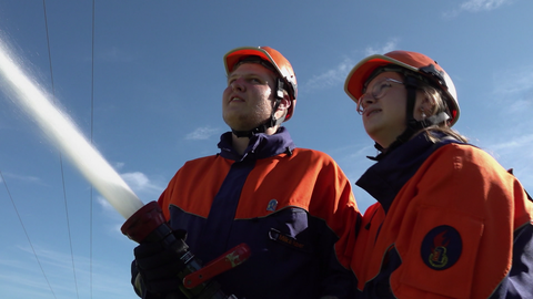 Zwei Jugendliche in Jugendfeuerwehr-Uniform. Einer hält einen Feuerwehrschlauch.