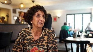 Tatjana Pannone sitzt in einem Café. Sie hat kurze, braune Locken und trägt ein Leoparden-Shirt.