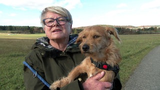 Gerlinde trägt eine Brille und hat einen Hund auf dem Arm