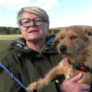 Gerlinde trägt eine Brille und hat einen Hund auf dem Arm