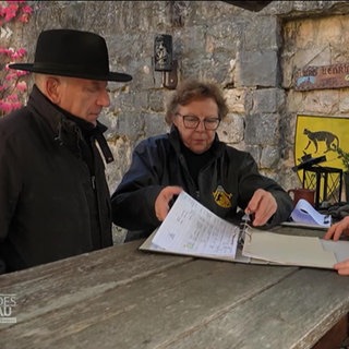 Ein älteres Ehepaar blättert mit ihrem Sohn in einer Burg durch einen Ordner