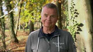 Ralf Wernicke steht vor herbtlich gefärbten Bäumen und lächelt in die Kamera.
