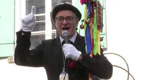 Ein "Fasnetslader" spricht mit Anzug, Hut und Mikro zu den Besuchern