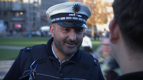 Luan steht in Polizeiuniform auf der Straße und spricht mit Passanten während seiner Präventionsstreife in Stuttgart.