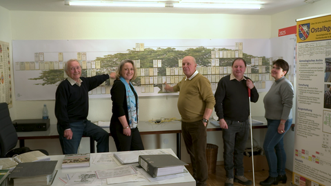 Eine Gruppe Ahnenforscher steht konzentriert vor einem großen Stammbaum.