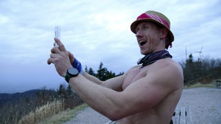Ultraläufer Daniel Hernes filmt sich selbst mit einem Handy. Sein Oberkörper ist nackt und er trägt einen Hut.