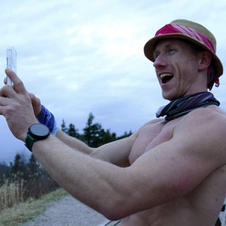 Ultraläufer Daniel Hernes filmt sich selbst mit einem Handy. Sein Oberkörper ist nackt und er trägt einen Hut.