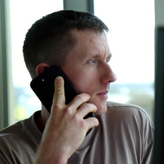 Ultraläufer Daniel Hernes sitzt an einem Computer im Büro. Er hat ein Handy am Ohr und telefoniert.