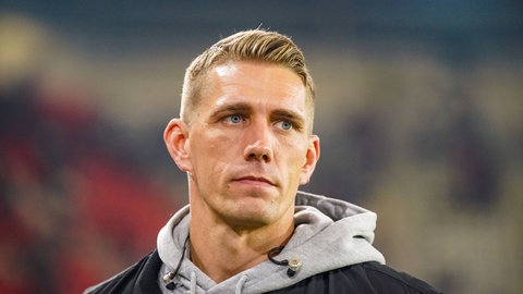 Nils Petersen, ehemaliger Stürmer des SC Freiburg, steht im Stadion. Er trägt einen grauen Kapuzenpullover und eine schwarze Jacke.