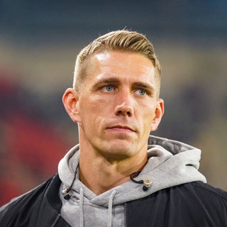 Nils Petersen, ehemaliger Stürmer des SC Freiburg, steht im Stadion. Er trägt einen grauen Kapuzenpullover und eine schwarze Jacke.